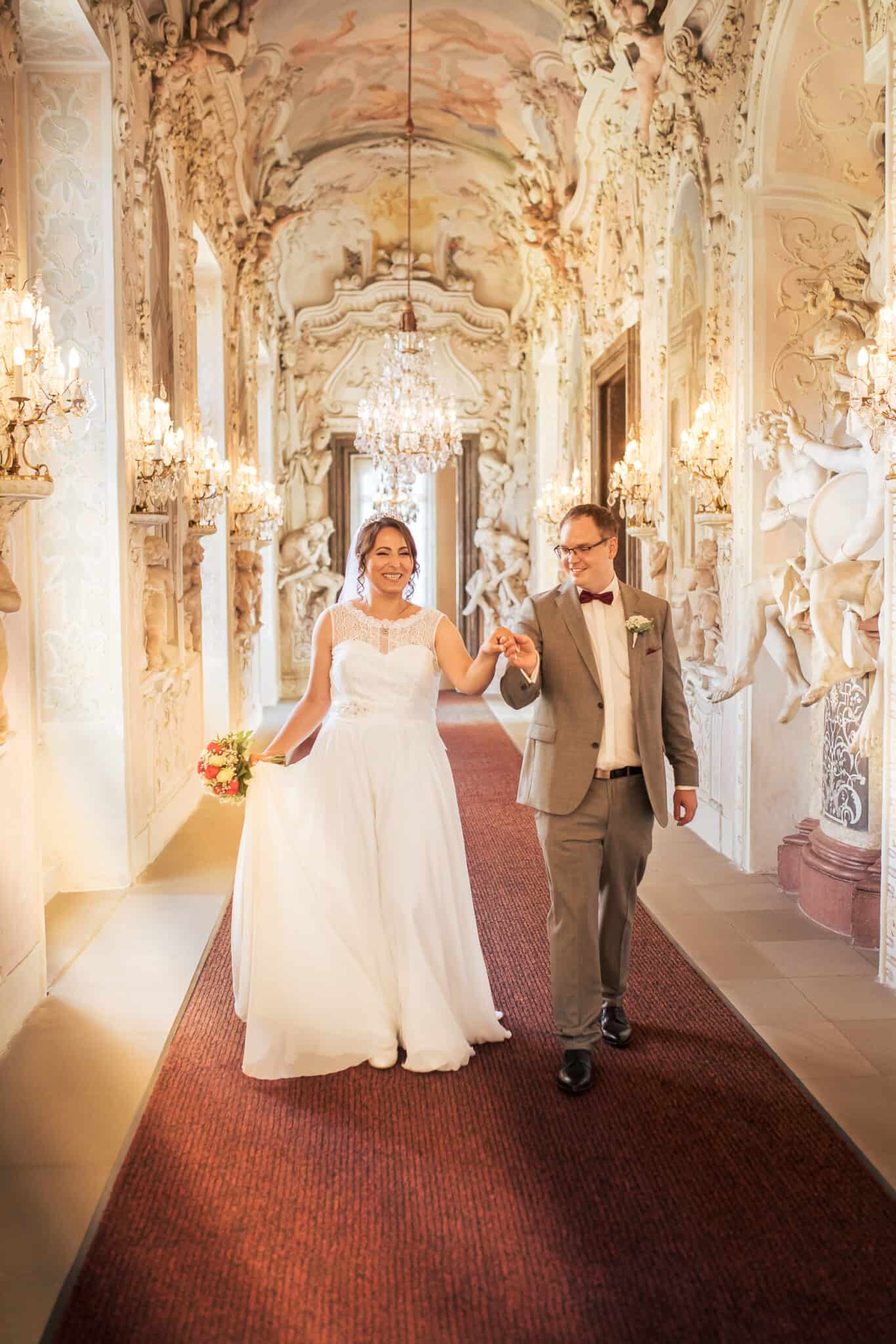 hochzeitsalben hochwertig hochzeitsfotograf Hochzeitsfotograf Ludwigsburg – Brautpaar im prunkvollen Schlossflur mit Kronleuchtern.