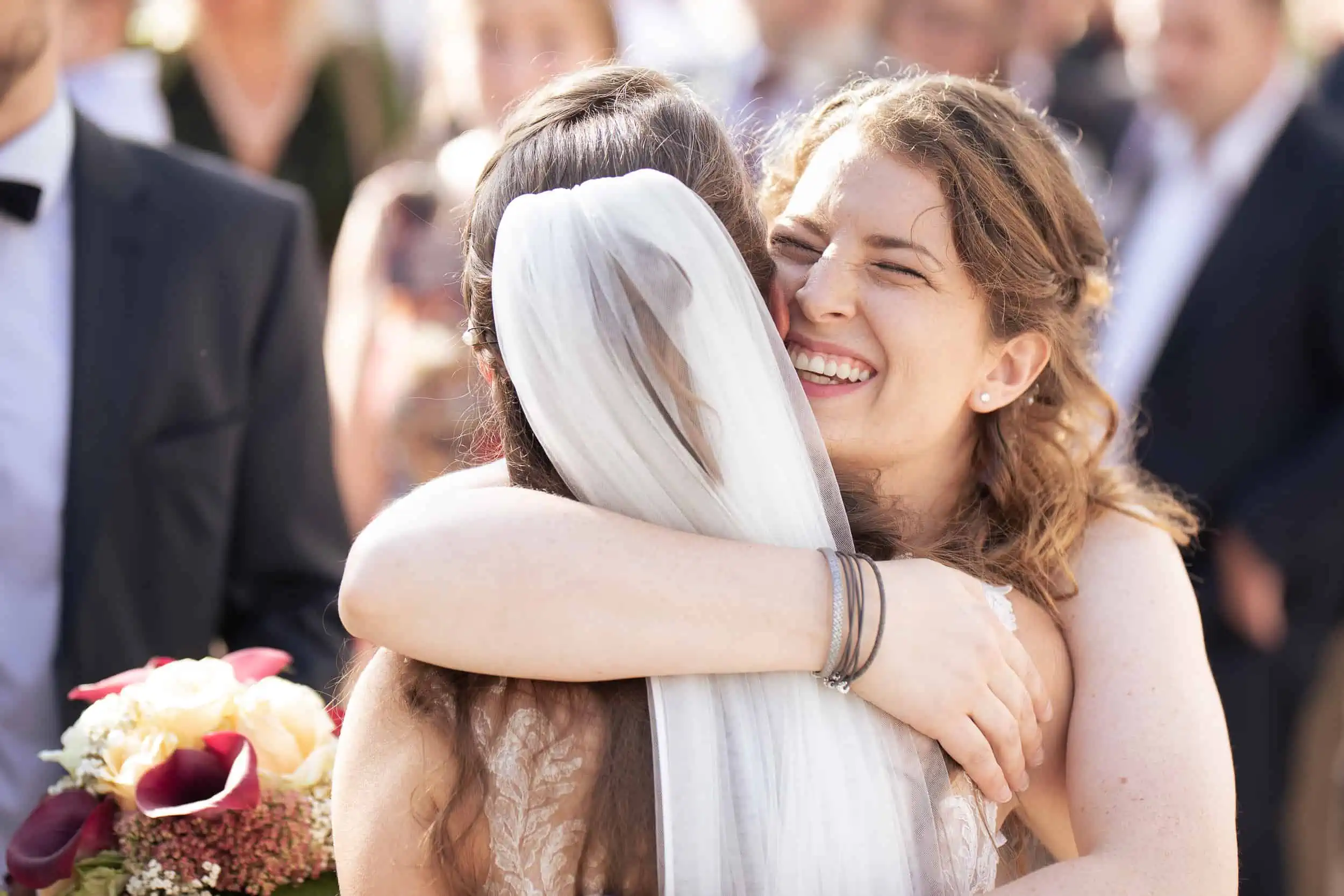 Glückliche Umarmung zwischen Braut und Freundin bei Hochzeit