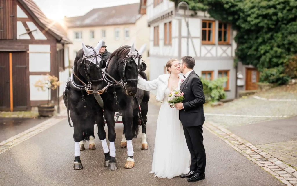 Brautpaar küsst sich vor Hochzeitskutsche mit zwei schwarzen Pferden in Waiblingen. Brautpaar küsst sich vor Hochzeitskutsche mit zwei schwarzen Pferden in Waiblingen.