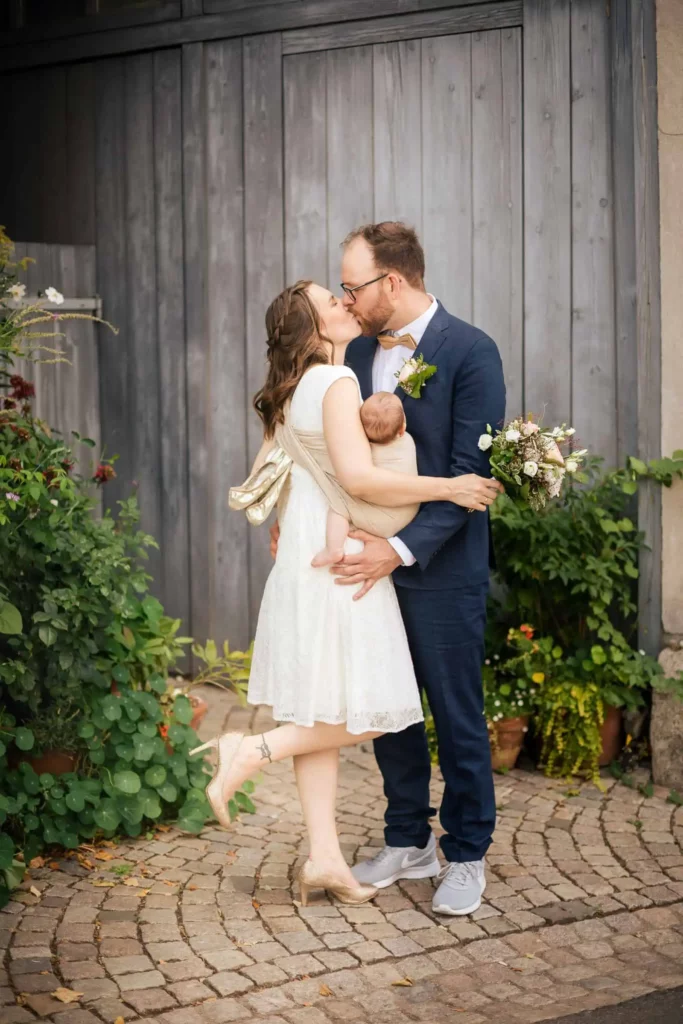 Hochzeitspaar küsst sich mit Baby im Arm bei Sommerhochzeit in Pforzheim Hochzeitspaar küsst sich mit Baby im Arm bei Sommerhochzeit in Pforzheim