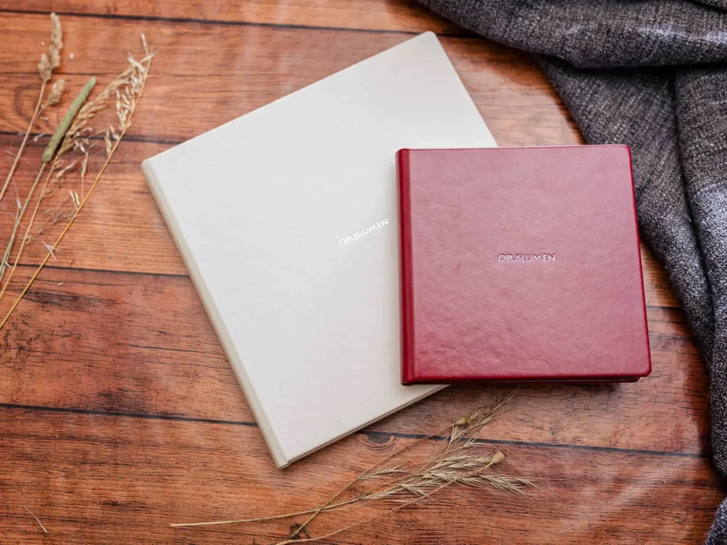 Zwei hochwertige Hochzeitsalben in Beige und Rot auf Holzhintergrund, stilvoll präsentiert.