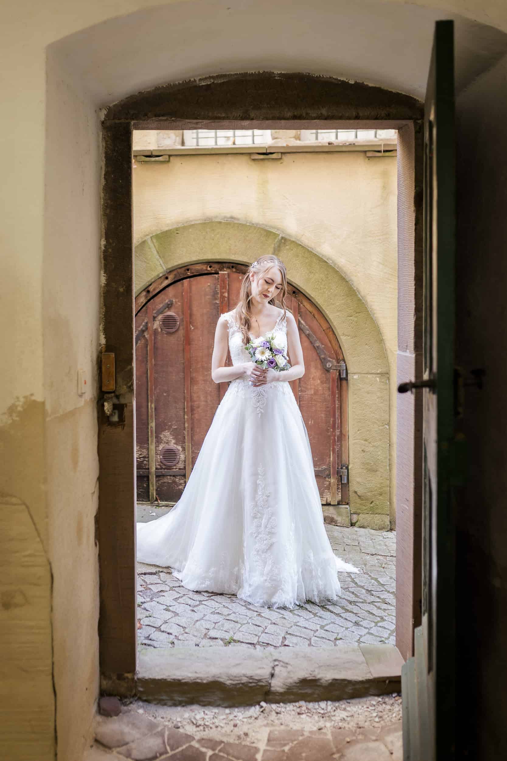 Fotograf Böblingen Empfehlung - Braut steht mit Blumenstrauß im Torbogen