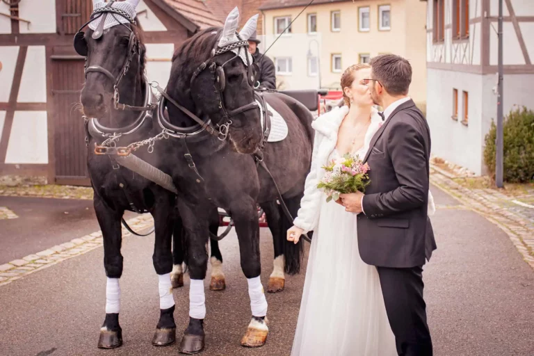 Brautpaar küsst sich vor der Pferdekutsche – rustikale Dorfhochzeit