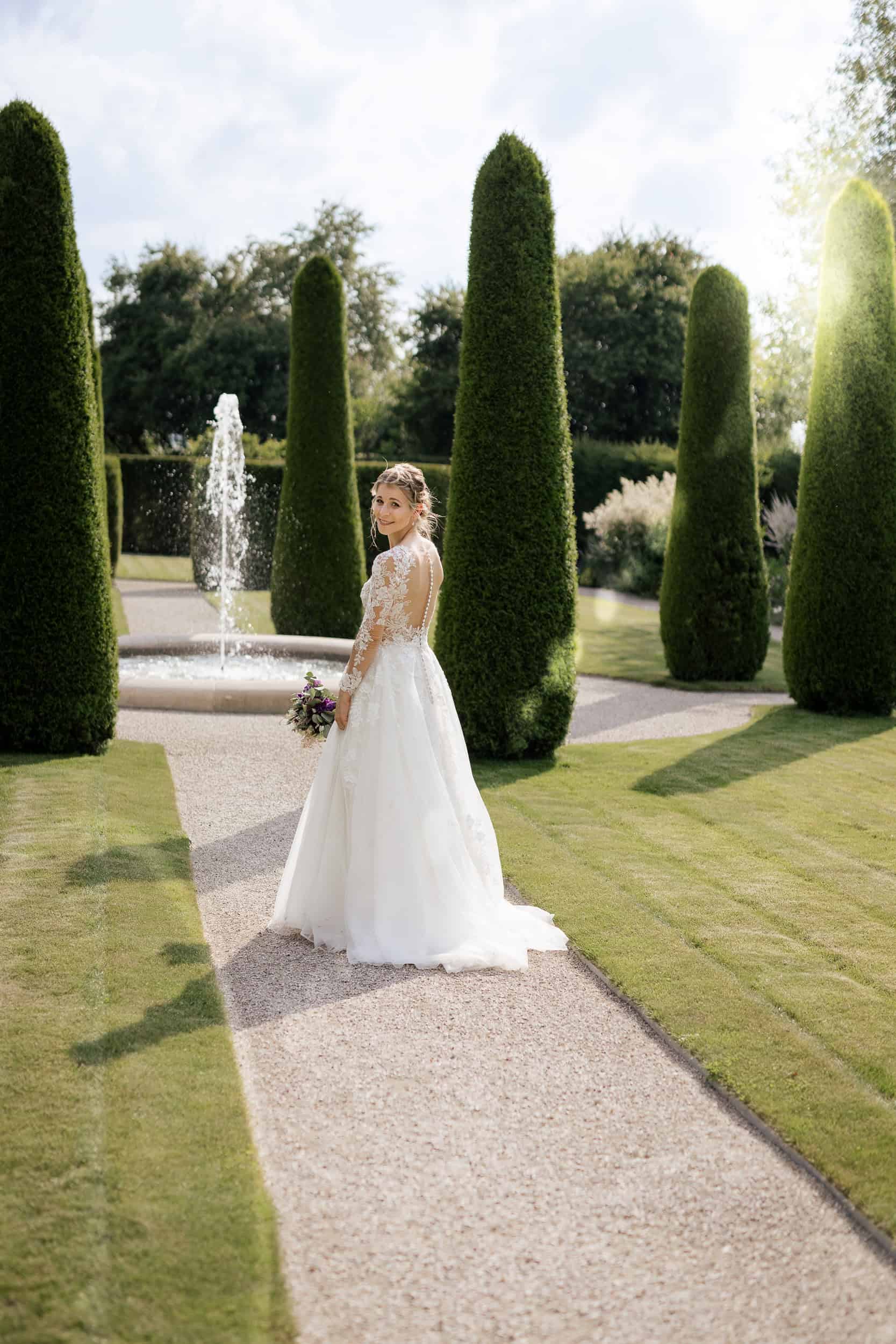 Hochzeitsfotograf Konstanz -   Braut in Hochzeitskleid im gepflegten Garten mit Springbrunnen und Topfgehölzen.
